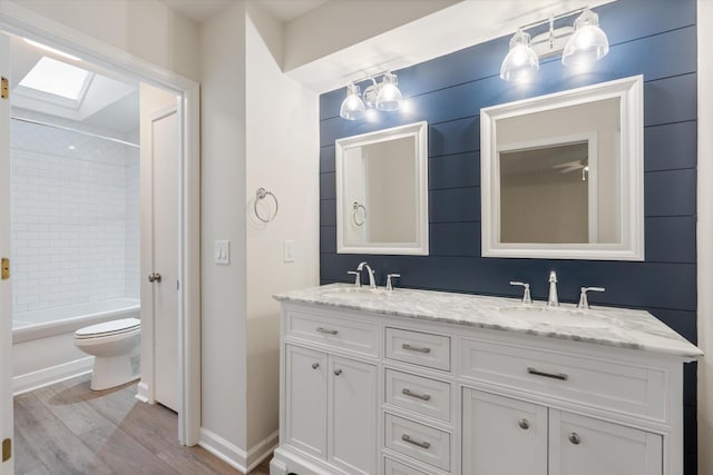 full bathroom featuring a skylight, tiled shower / bath combo, wood-type flooring, toilet, and vanity