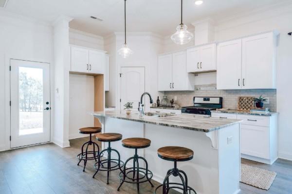 kitchen with white cabinets, an island with sink, pendant lighting, and range