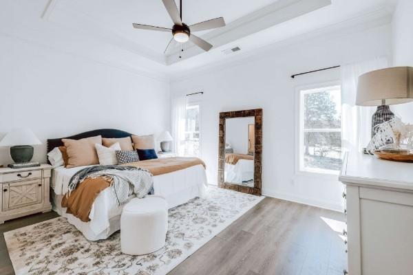 bedroom featuring a tray ceiling, ceiling fan, ornamental molding, and light wood-type flooring