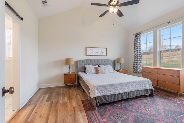 bedroom featuring a barn door, ceiling fan, light hardwood / wood-style flooring, and vaulted ceiling