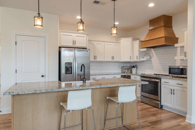 kitchen with white cabinetry, hanging light fixtures, premium range hood, appliances with stainless steel finishes, and light wood-type flooring