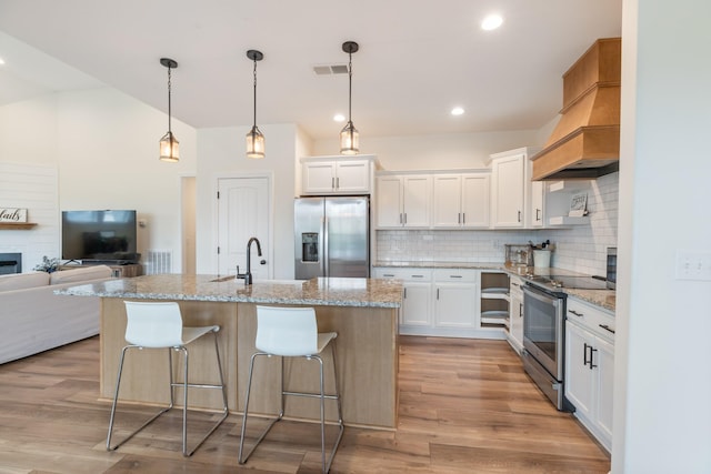 kitchen featuring stainless steel appliances, an island with sink, decorative light fixtures, decorative backsplash, and white cabinets