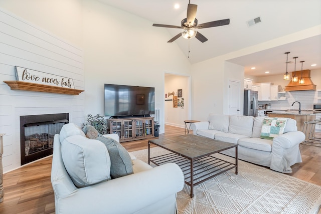 living room with a fireplace, high vaulted ceiling, light hardwood / wood-style flooring, and ceiling fan