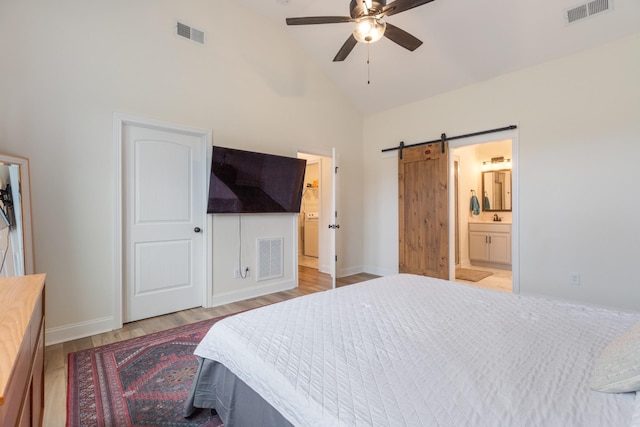 bedroom featuring ensuite bath, ceiling fan, a barn door, high vaulted ceiling, and light hardwood / wood-style floors