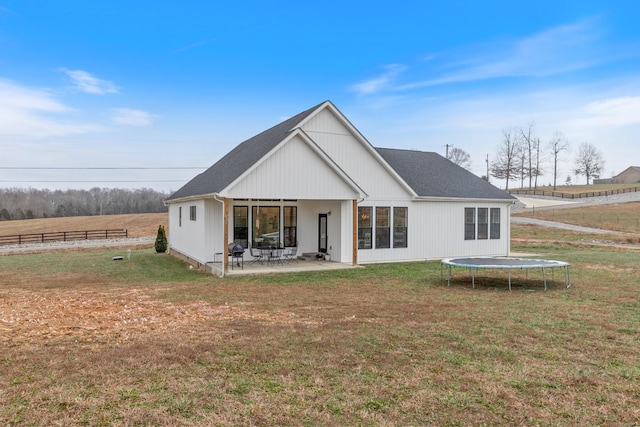 rear view of property with a lawn, a patio area, a rural view, and a trampoline