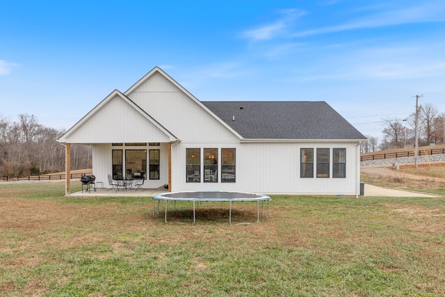 rear view of property with a lawn, a trampoline, and a patio