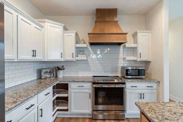 kitchen with light stone countertops, tasteful backsplash, premium range hood, stainless steel appliances, and white cabinetry