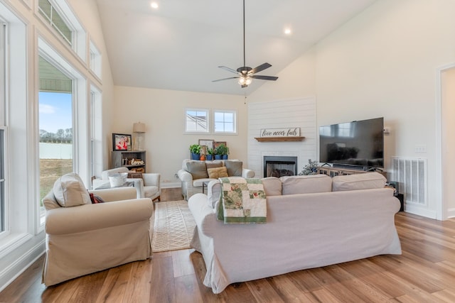 living room featuring a fireplace, light wood-type flooring, high vaulted ceiling, and ceiling fan