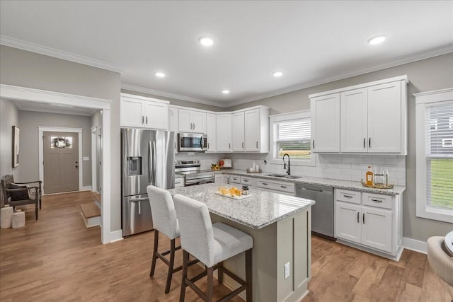 kitchen featuring light stone countertops, sink, stainless steel appliances, a kitchen island, and white cabinets