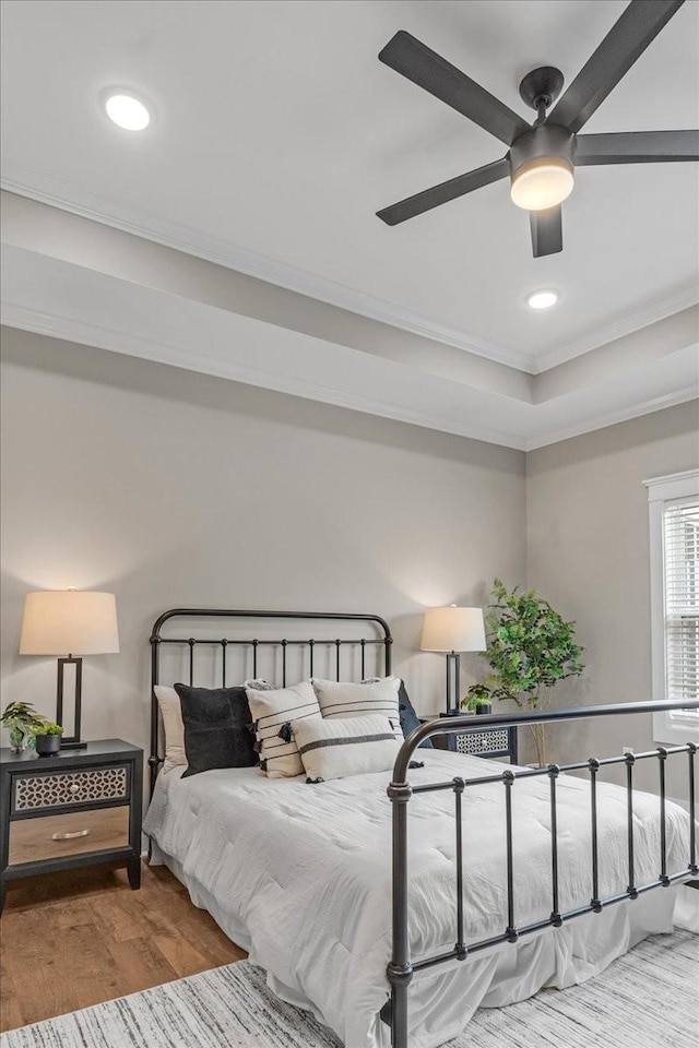 bedroom with a raised ceiling, ceiling fan, wood-type flooring, and ornamental molding