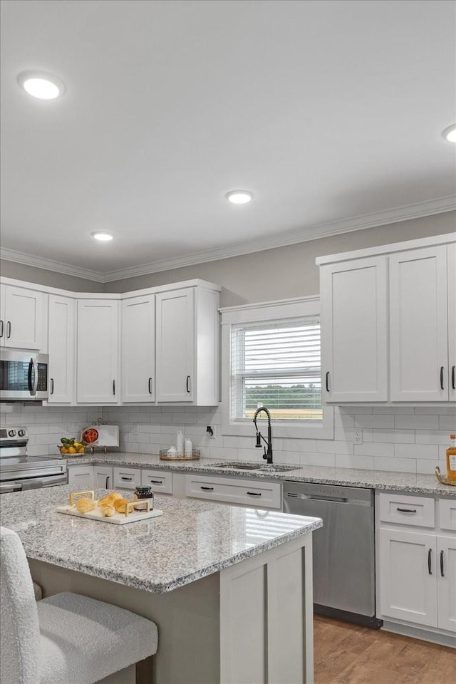 kitchen with white cabinets, sink, light stone countertops, appliances with stainless steel finishes, and light hardwood / wood-style floors