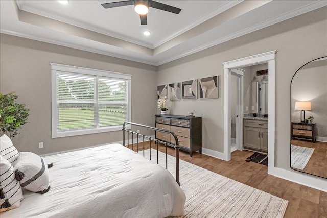 bedroom with crown molding, ensuite bath, hardwood / wood-style flooring, ceiling fan, and a tray ceiling