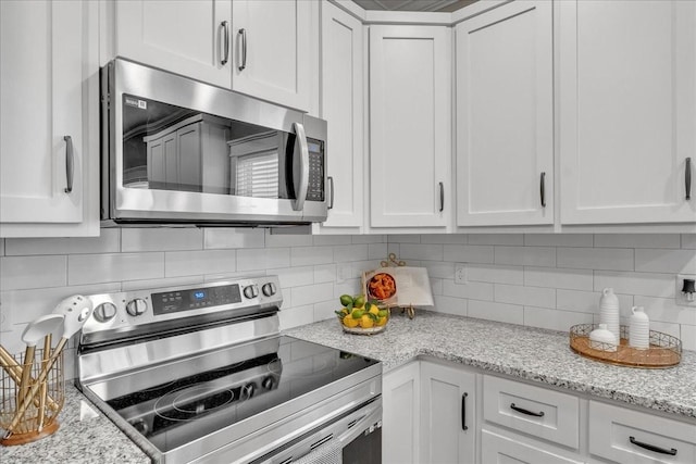 kitchen featuring decorative backsplash, appliances with stainless steel finishes, white cabinetry, and light stone counters