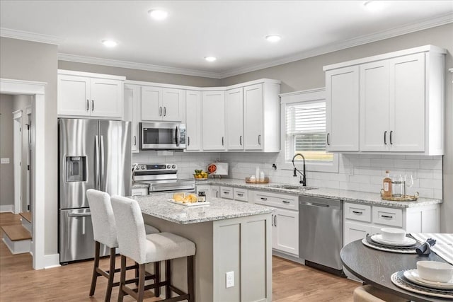 kitchen featuring light stone countertops, appliances with stainless steel finishes, sink, white cabinets, and a center island