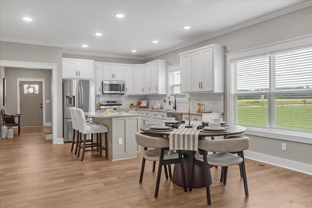 kitchen with light stone countertops, white cabinetry, a center island, stainless steel appliances, and light hardwood / wood-style floors