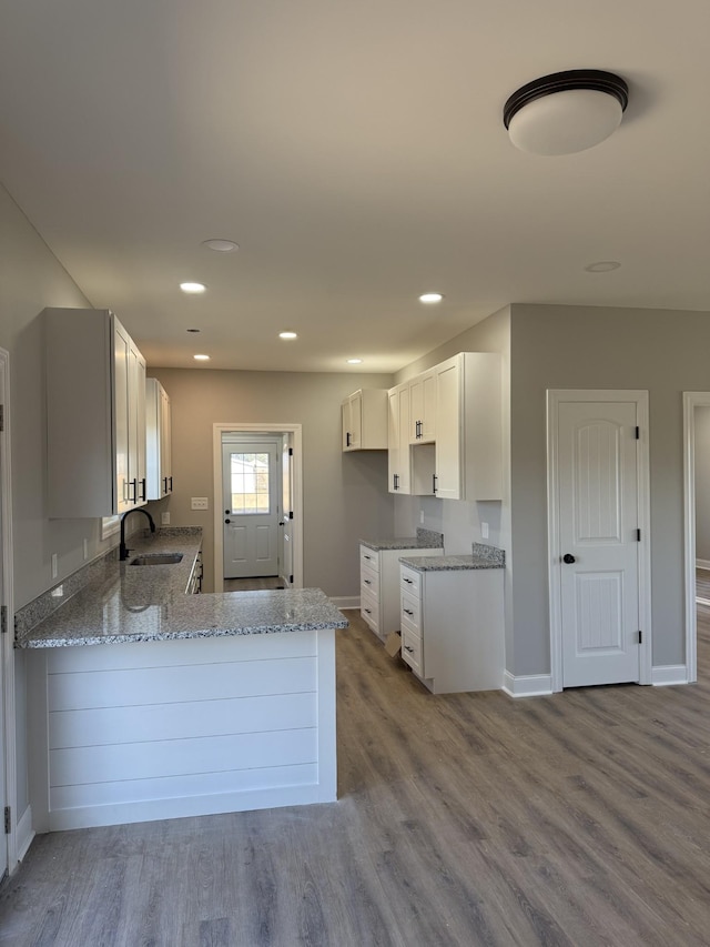 kitchen featuring white cabinetry, sink, light stone countertops, kitchen peninsula, and light wood-type flooring