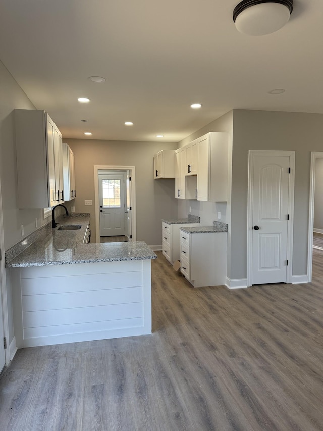 kitchen featuring kitchen peninsula, sink, light stone countertops, light hardwood / wood-style floors, and white cabinetry