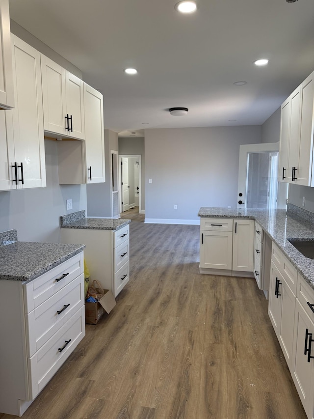 kitchen featuring kitchen peninsula, light stone counters, dark hardwood / wood-style flooring, and white cabinets