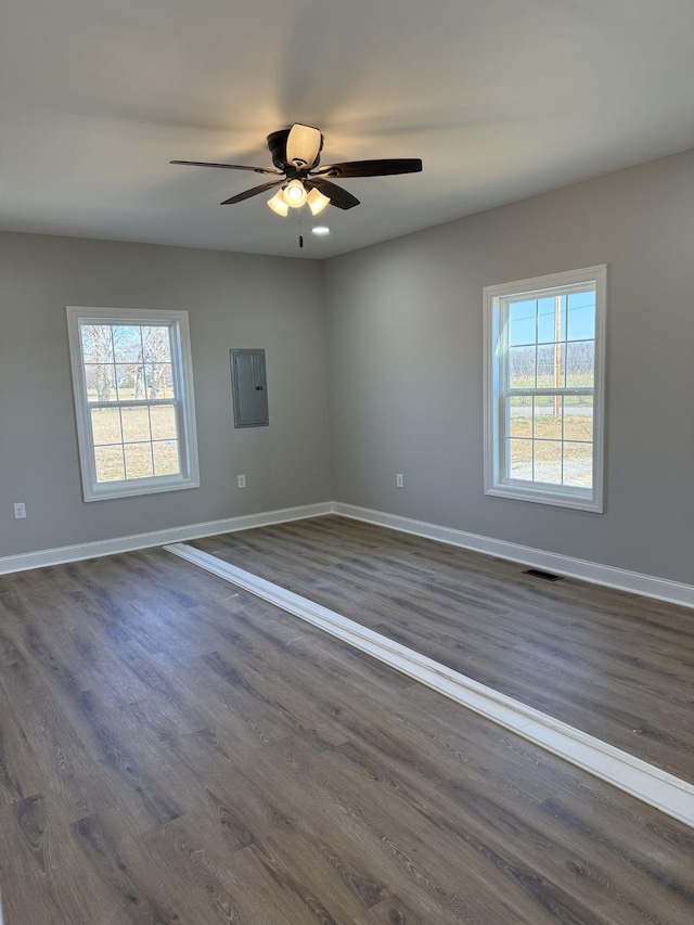 empty room featuring electric panel, ceiling fan, dark hardwood / wood-style flooring, and plenty of natural light