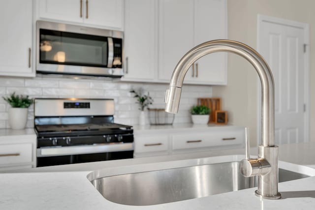 kitchen featuring light stone countertops, backsplash, stainless steel appliances, sink, and white cabinetry