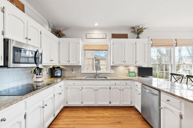 kitchen with stainless steel appliances, white cabinets, sink, and light stone countertops