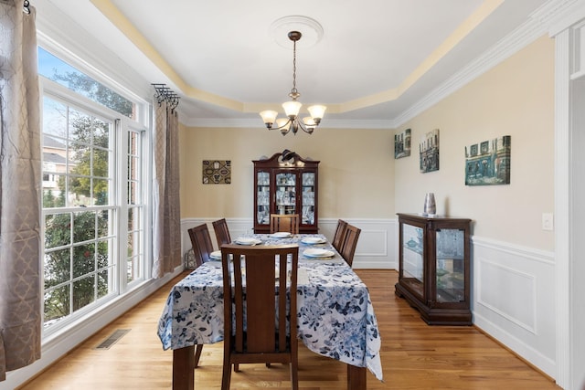 dining space with light hardwood / wood-style flooring, a wealth of natural light, a chandelier, and a tray ceiling