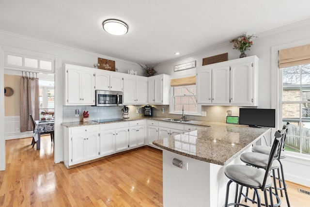 kitchen with kitchen peninsula, a kitchen bar, stone countertops, white cabinetry, and sink