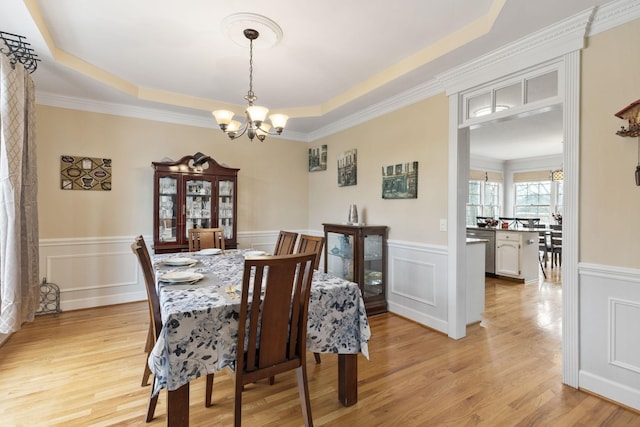 dining room featuring ornamental molding, a raised ceiling, a notable chandelier, and light hardwood / wood-style flooring