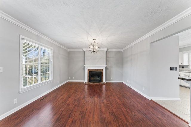 unfurnished living room featuring hardwood / wood-style floors, a notable chandelier, ornamental molding, and a brick fireplace