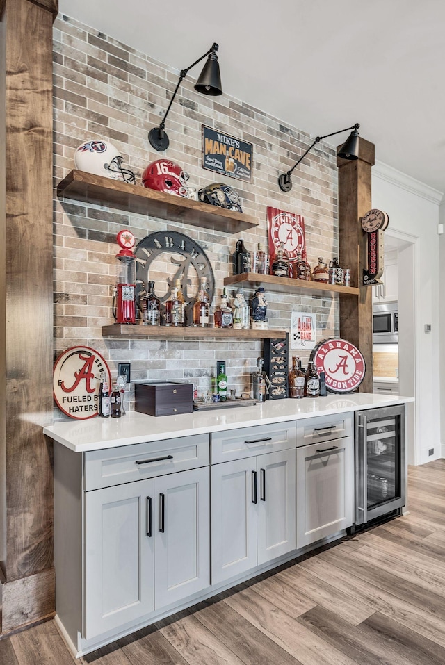 bar with light wood-type flooring, stainless steel microwave, gray cabinets, and beverage cooler