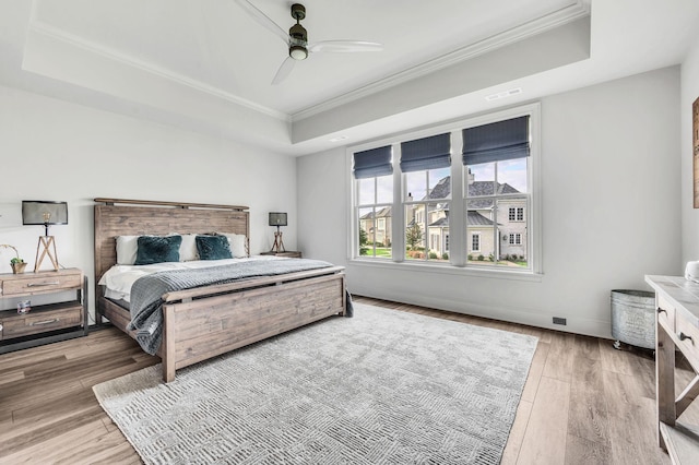 bedroom featuring hardwood / wood-style floors, ceiling fan, crown molding, and a tray ceiling