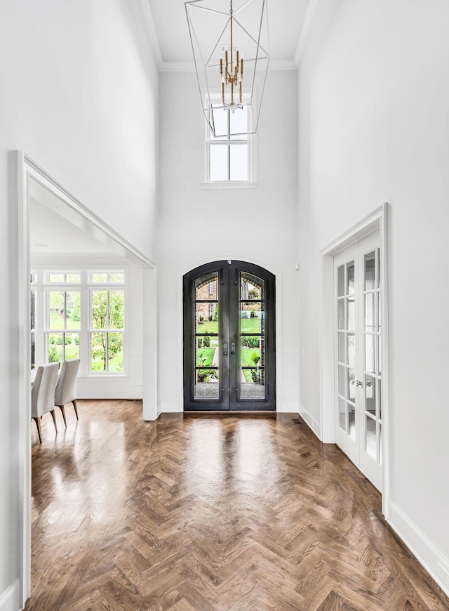 foyer entrance with french doors, dark parquet floors, crown molding, an inviting chandelier, and a high ceiling