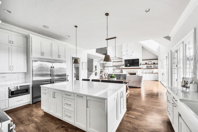 kitchen featuring white cabinets, built in appliances, decorative light fixtures, and a kitchen island