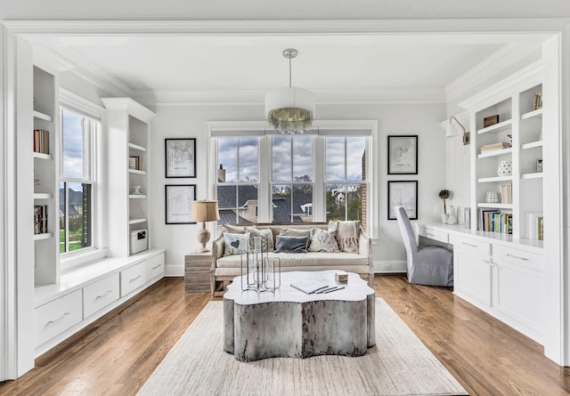 living area with built in shelves, crown molding, built in desk, hardwood / wood-style flooring, and an inviting chandelier