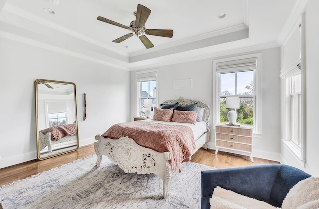 bedroom with light wood-type flooring, a raised ceiling, ceiling fan, and crown molding