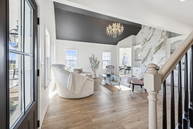 living room with lofted ceiling, built in features, a notable chandelier, and light hardwood / wood-style floors