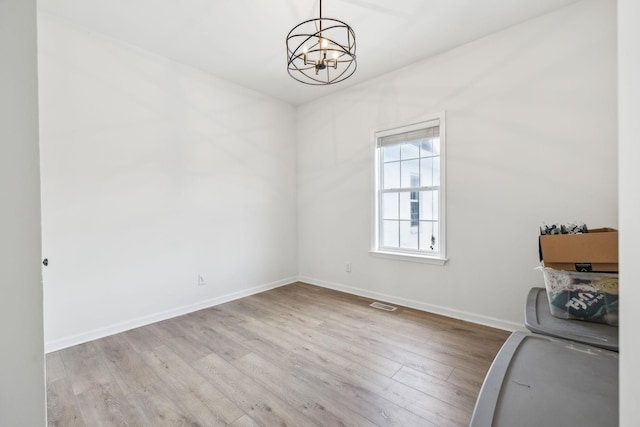 spare room with light wood-type flooring and an inviting chandelier