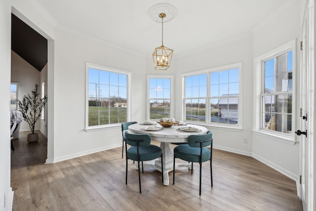 dining space featuring vaulted ceiling, a notable chandelier, ornamental molding, and light hardwood / wood-style flooring