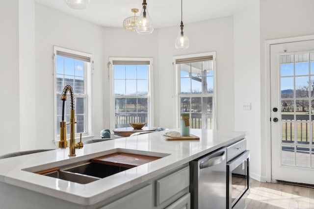 kitchen with dishwasher, light stone counters, hanging light fixtures, and sink