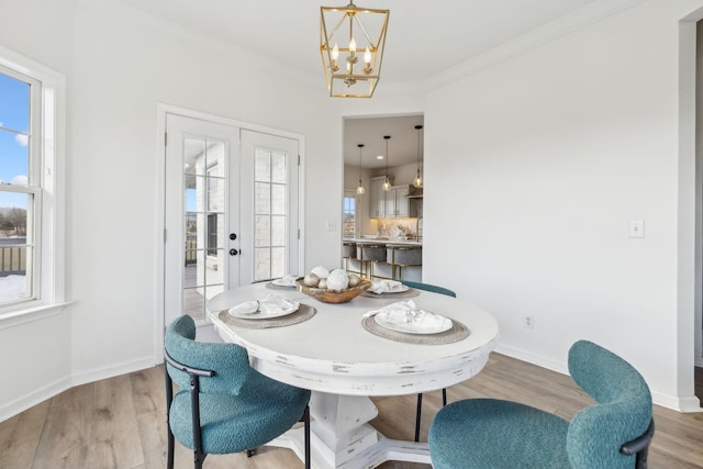 dining space featuring light wood-type flooring, french doors, a notable chandelier, and crown molding