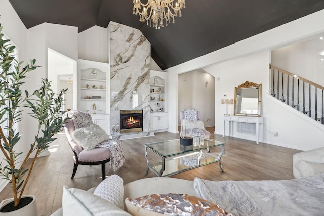 living room featuring hardwood / wood-style floors, high vaulted ceiling, built in shelves, a high end fireplace, and a chandelier