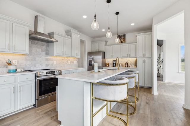 kitchen with appliances with stainless steel finishes, backsplash, a kitchen island with sink, wall chimney range hood, and a breakfast bar