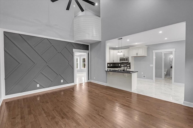 unfurnished living room featuring ceiling fan, sink, hardwood / wood-style floors, and a high ceiling