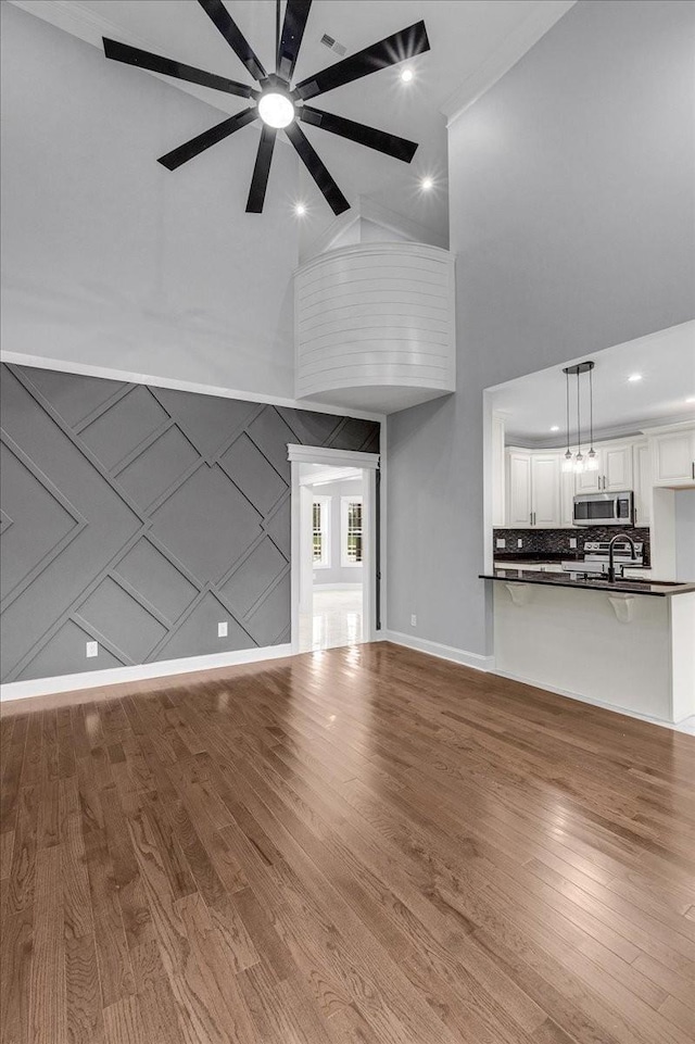 unfurnished living room with a towering ceiling, light hardwood / wood-style floors, ceiling fan, and ornamental molding