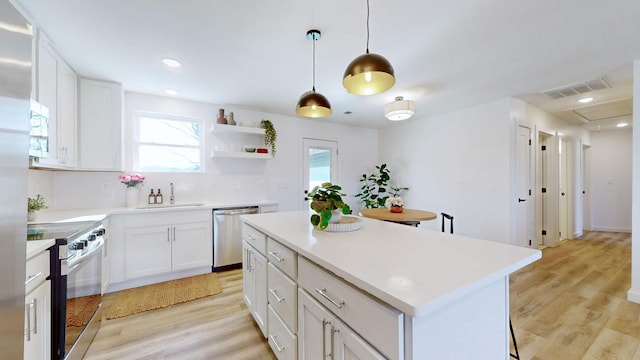 kitchen with hanging light fixtures, white cabinets, light hardwood / wood-style floors, a kitchen island, and appliances with stainless steel finishes