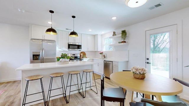 kitchen with hanging light fixtures, white cabinets, stainless steel appliances, and a kitchen island