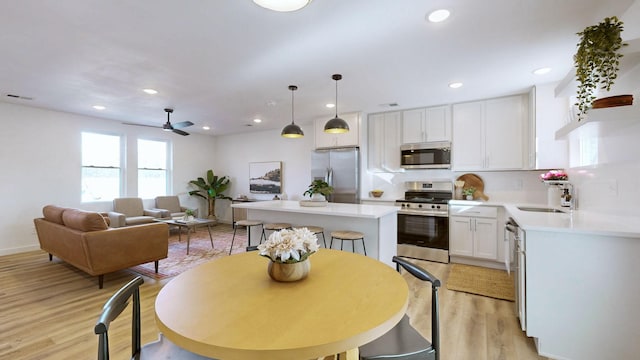 kitchen with light wood-type flooring, stainless steel appliances, decorative light fixtures, a center island, and white cabinetry