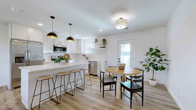 kitchen featuring stainless steel appliances, white cabinetry, hanging light fixtures, and a kitchen island