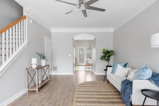 living room with wood-type flooring, ceiling fan with notable chandelier, and crown molding