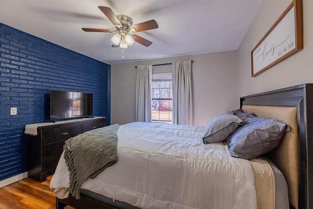 bedroom with light wood-type flooring, ceiling fan, and brick wall